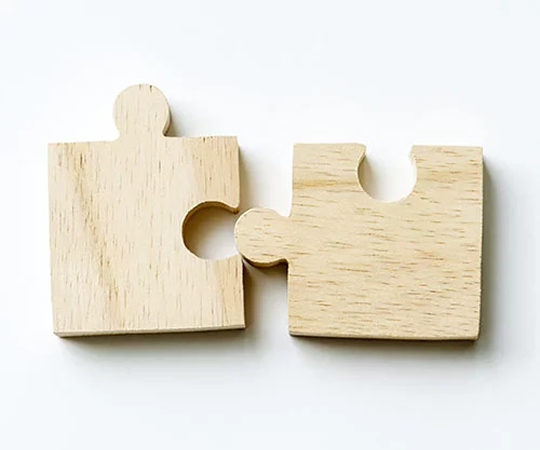 Twee lichte, houten puzzelstukjes op een witte achtergrond, die gedeeltelijk met elkaar verbonden zijn.